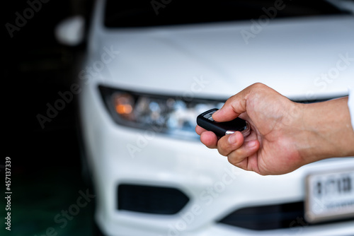 Hand of a man holding and push remote control of white car, technology transportation safety concept