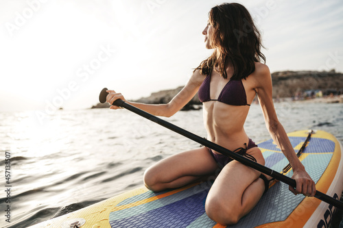 Beautiful young woman sitting on a stand up paddle board in sea