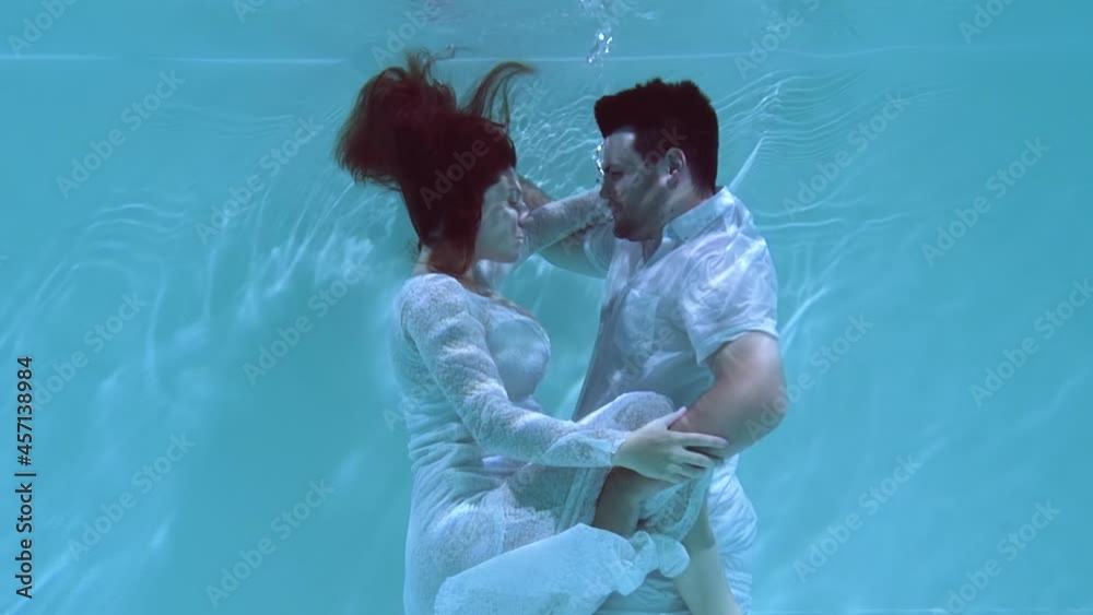 Man and a woman are dancing underwater. People dive in clothes under the water hugging each other.