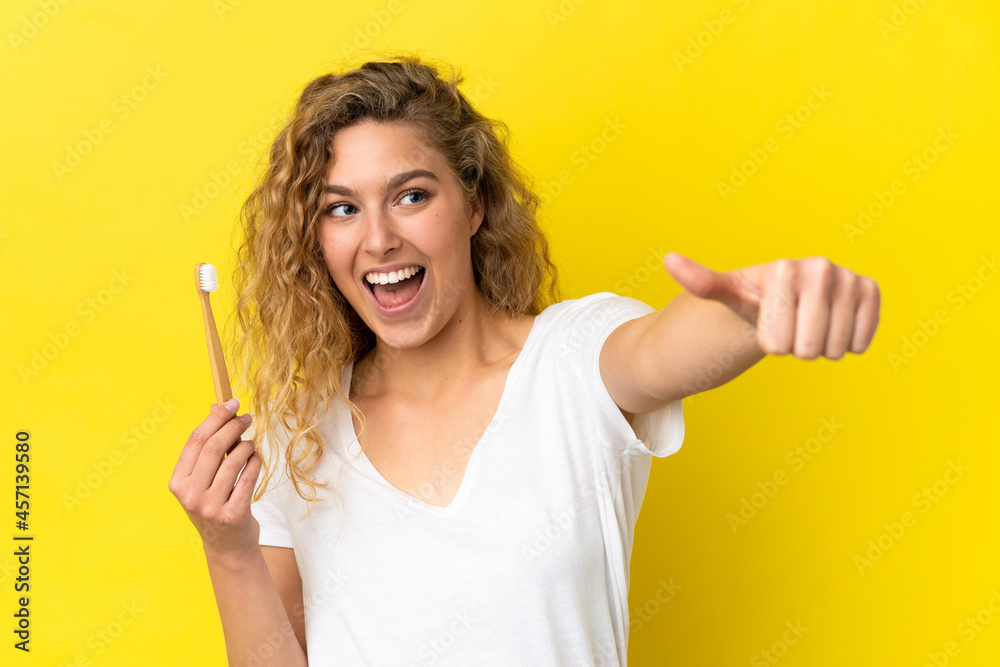 Young caucasian woman holding a brushing teeth isolated on yellow background giving a thumbs up gesture Young caucasian woman holding a brushing teeth isolated on yellow background giving a thumbs up gesture