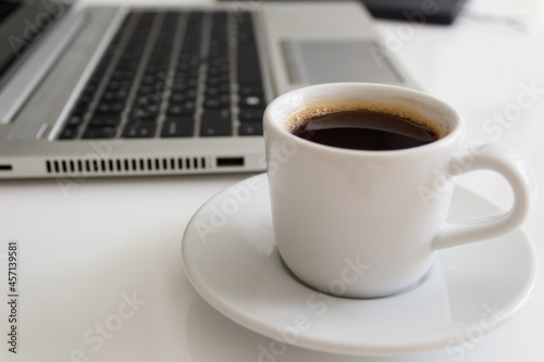 The concept of a workplace with coffee in a neat white mug  a laptop and a notebook with a pen on a modern white office desk. Easy to use. Minimalism. Side view.