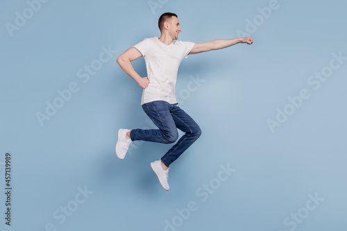 Full size profile side photo of excited man jumping fly air superhero isolated over blue color background