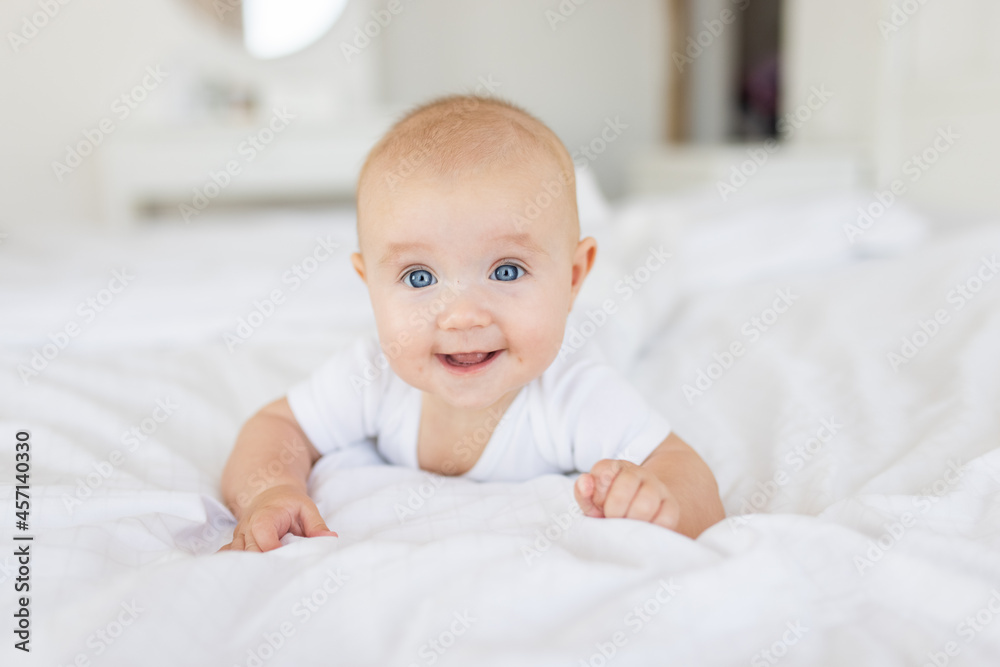 Portrait of cute and smiling four month old baby girl playing on the bed in her room. Happy and dry kid. 