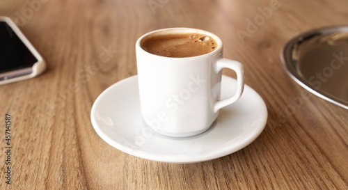 Traditional Turkish coffee in small white cup on wooden table