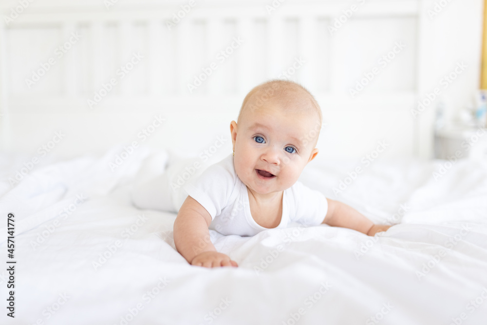Portrait of cute and smiling four month old baby girl playing on the bed in her room. Happy and dry kid. 