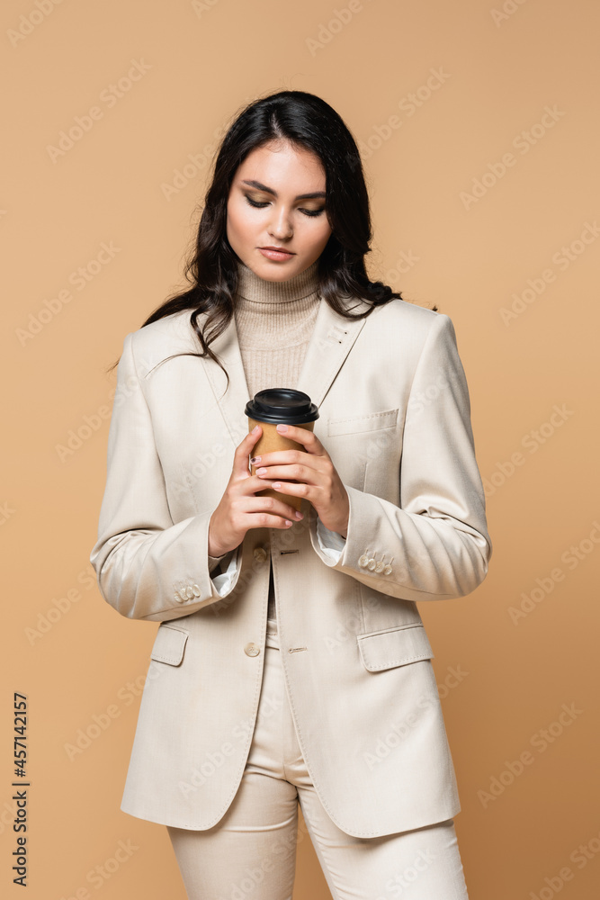 young woman in turtleneck and suit holding paper cup isolated on beige young woman in turtleneck and suit holding paper cup isolated on beige