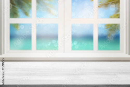 Blank white wood table top and window with  blur sea sand and palm leaves background Product Display stand