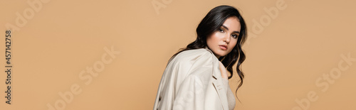 pretty young model holding blazer while posing isolated on beige, banner