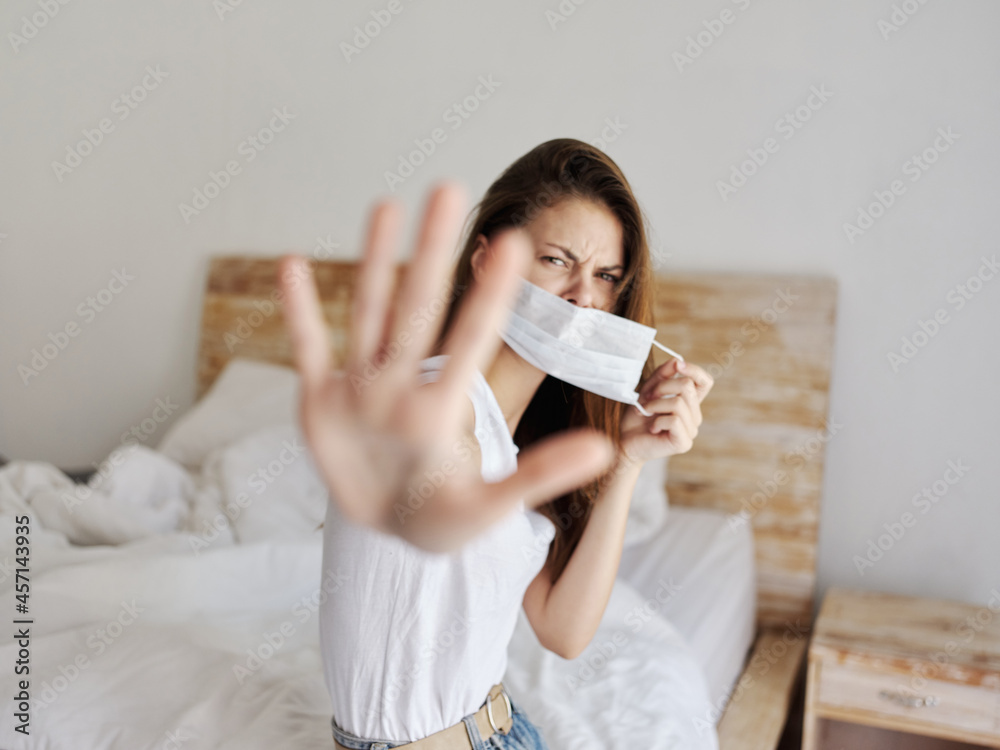 pretty woman with medical mask on face covered with hands sitting on bed indoors pretty woman with medical mask on face covered with hands sitting on bed indoors