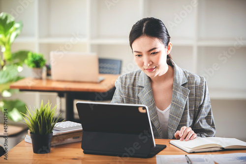 Asian girls are enjoying business video call, sitting at desk, using laptop computer, having video chat, waving
