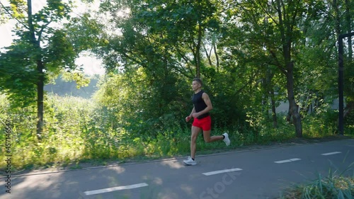 Wallpaper Mural Slow motion fit man in summer sportswear jogging in park, sun shining through trees, cable cars on background. Tracking shot runner training outside. Concept of fitness Torontodigital.ca