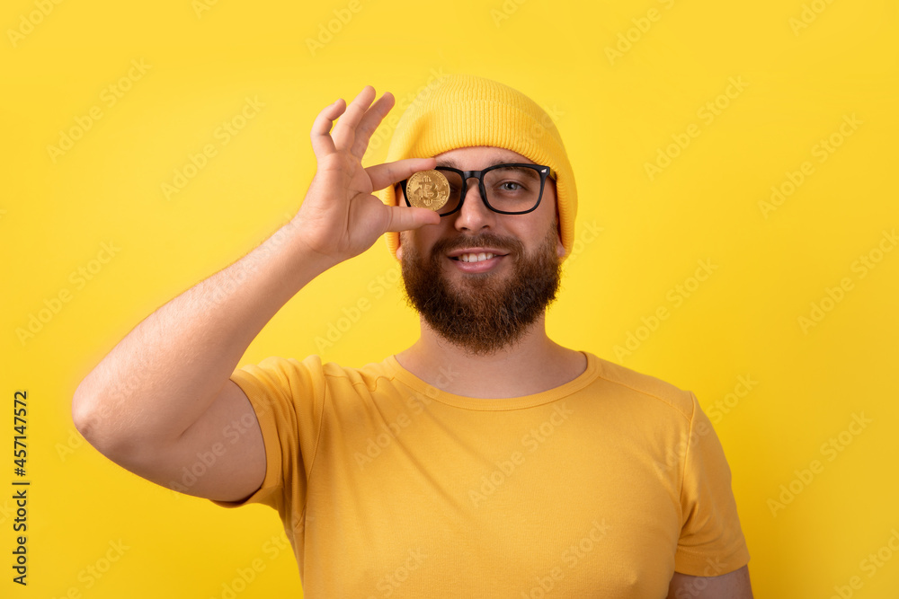 man covering eye with bitcoin over yellow background