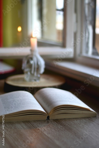 Open book and lit candle on a table. Selective focus.