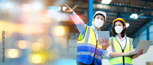Team engineers and foreman wear a mask, hard hat, and vest. Standing consult discuss industrial production management. Explaining job details through laptops and tablets in factories or warehouses.
