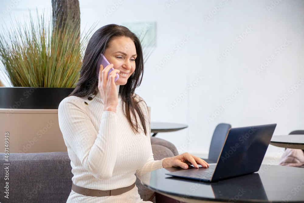 beautiful middle-aged woman smiling talking on the phone at laptop in office beautiful middle-aged woman smiling talking on the phone at laptop in office