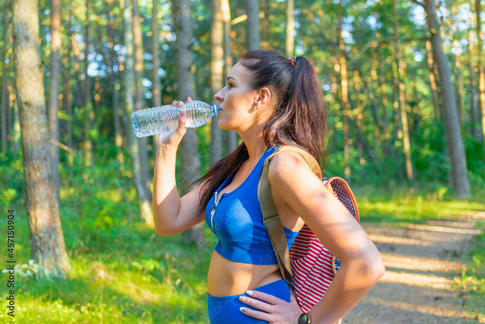 attractive happy young woman hiker with backpack drinking bottled water walking on summer forest trail summer landscape attractive happy young woman hiker with backpack drinking bottled water walking on summer forest trail summer landscape