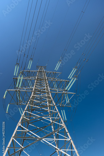 Close-up view of a high-voltage power line support with glass insulators on a blue sky background.