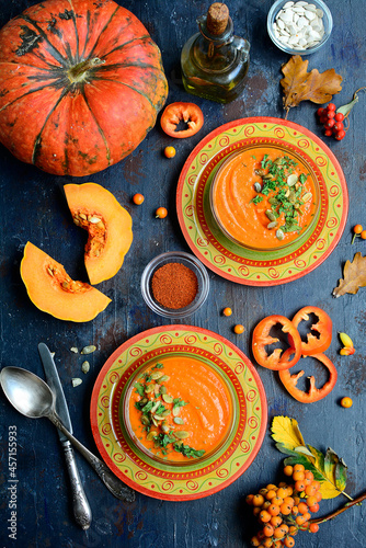 Two serving orange plates with pumpkin soup - mashed potatoes, spices, herbs, pumpkin on a dark blue background. Vertical. Top view