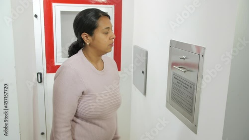 A Hispanic woman is putting a black plastic trash bag through a garbage chute photo