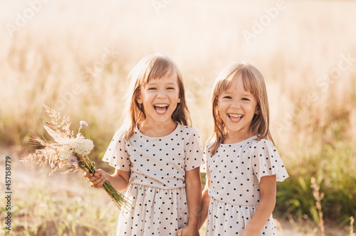 Two little happy identical twin girls playing together in nature in summer. Girls friendship and youth concept. Active children's lifestyle.