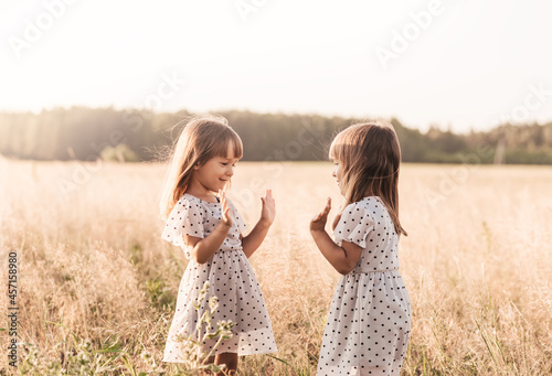 Two little happy identical twin girls playing together in nature in summer. Girls friendship and youth concept. Active children's lifestyle. photo