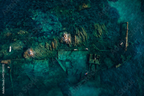 View from above, stunning aerial view of some people swimming and snorkeling around the Chrisso wreck lying on the bottom of the sea. Sardinia, Italy.