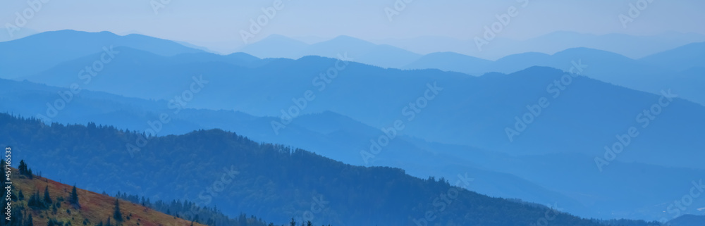 High peaks of blue mountain range landscape with fog. Horizontal image.