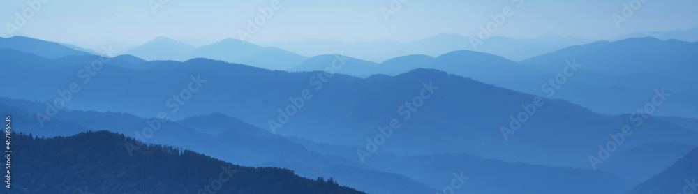 High peaks of blue mountain range landscape with fog and forest. Ukraine, Carpathians. Horizontal image.