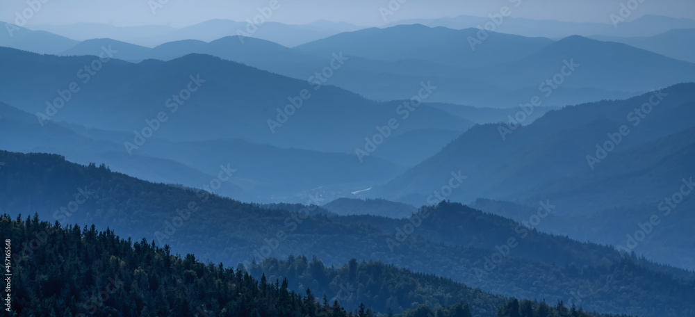 High peaks of beautiful dark blue mountain range landscape with fog and forest. Ukraine, Carpathians.