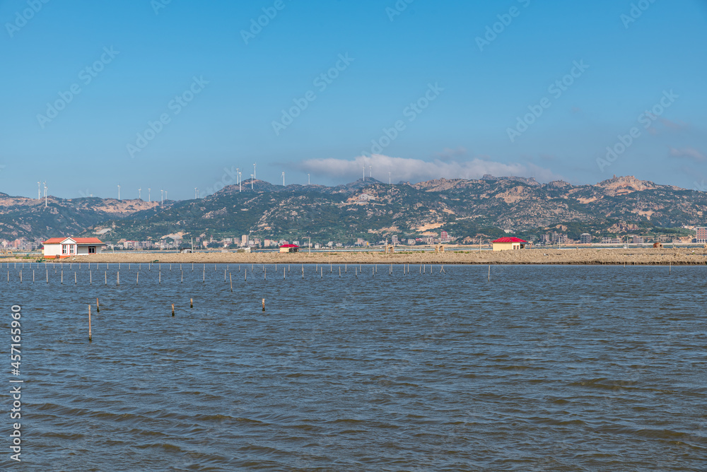 The coastline under the blue sky, opposite the sea are mountains and wind power