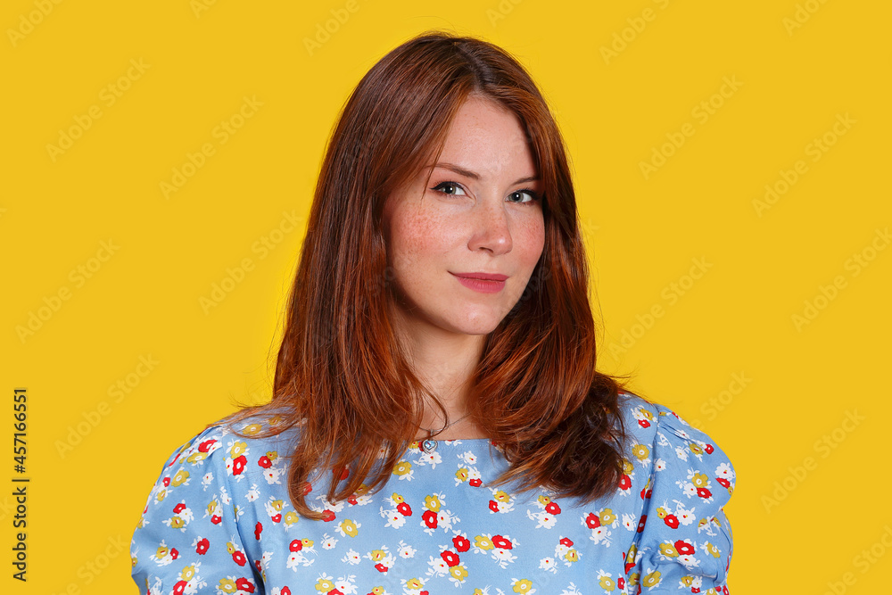Portrait of a beautiful red-haired model on a yellow background. The girl with long red hair smiles. Blue dress with patterns on a young woman. Modern fashion and comfortable clothing Portrait of a beautiful red-haired model on a yellow background. The girl with long red hair smiles. Blue dress with patterns on a young woman. Modern fashion and comfortable clothing