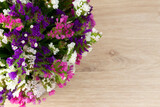 A bouquet of colorful dried flowers on a wooden background . The statitse is white, pink, purple.