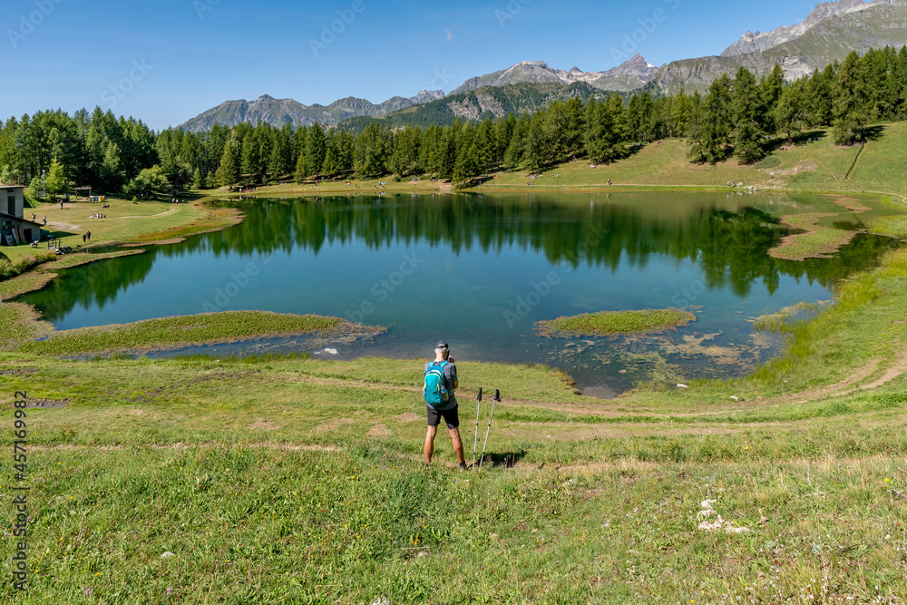 A man keen on trekking makes a stop near Lake Lod to take photos and videos with his smartphone, Aosta Valley, Italy