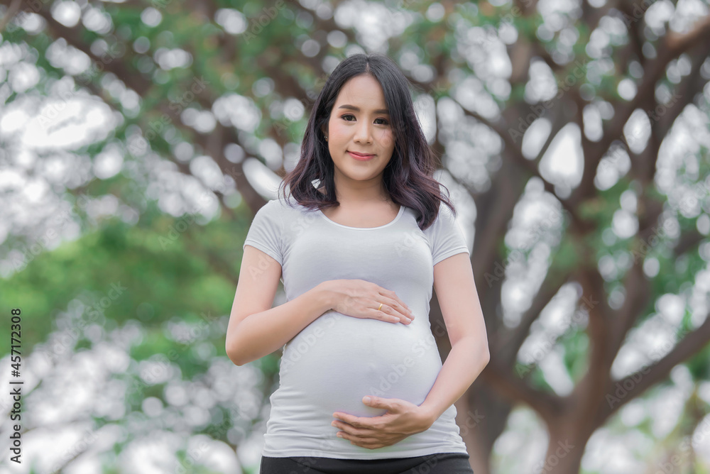 Portrait of asian Beautiful pregnant woman at the park,Thailand people,Happy woman concept,Her use hand touch her belly,Mother day concept