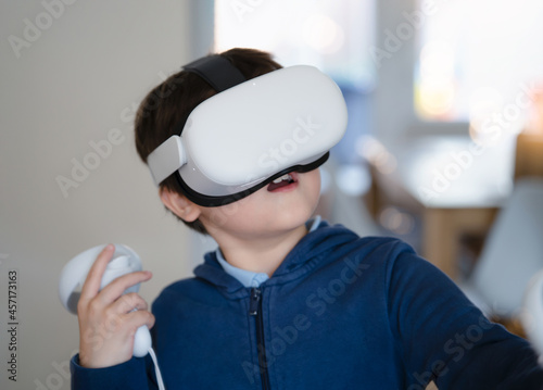 Amazed young kid wearing virtual reality goggles. Emotional Boy playing video games looking in VR headset. Portrait of Mixed race boy experiencing 3D gadget in living room.