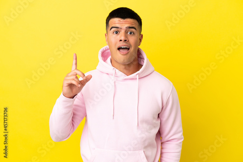 Young handsome man over isolated yellow background thinking an idea pointing the finger up