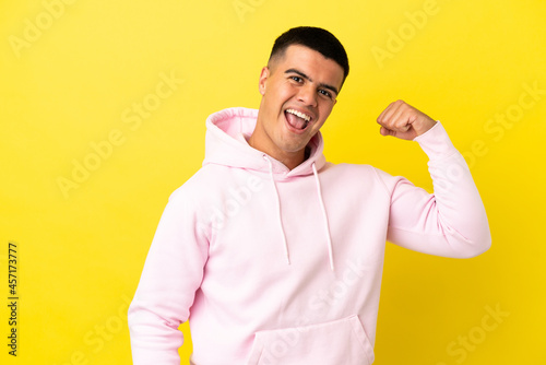 Young handsome man over isolated yellow background doing strong gesture