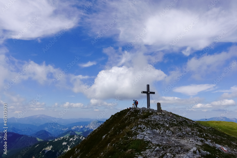 cross on the summit from a mountain with hikers and wide view