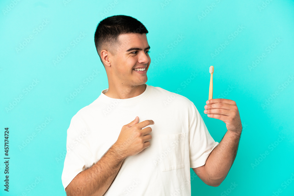 Fototapeta premium Young handsome man brushing teeth over isolated blue background looking to the side and smiling