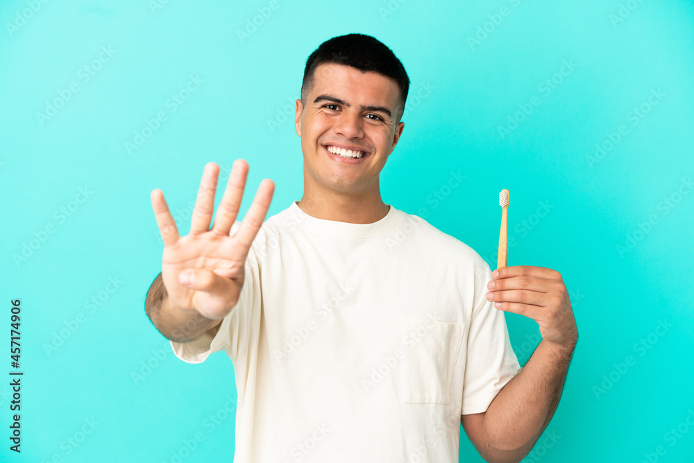 Young handsome man brushing teeth over isolated blue background happy and counting four with fingers
