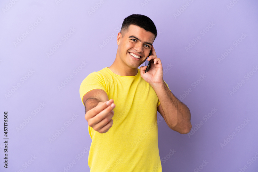 Fototapeta premium Young handsome man using mobile phone over isolated purple background making money gesture