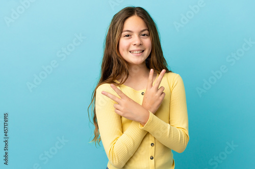 Little caucasian girl isolated on blue background smiling and showing victory sign