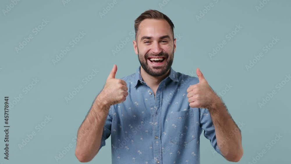 Excited cheerful charismatic delight ecstatic young brunet bearded man 20s wears denim shirt showing thumb up like gesture isolated on pastel light blue background. People emotions lifestyle concept Excited cheerful charismatic delight ecstatic young brunet bearded man 20s wears denim shirt showing thumb up like gesture isolated on pastel light blue background. People emotions lifestyle concept