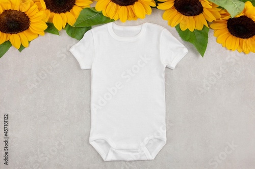 White baby girl or boy bodysuit mockup flat lay with sunflowers on gray concrete background. Design onesie template, print presentation mock up. Top view.