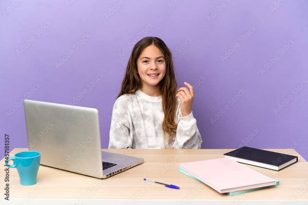 Little student girl in a workplace with a laptop isolated on purple background laughing Little student girl in a workplace with a laptop isolated on purple background laughing