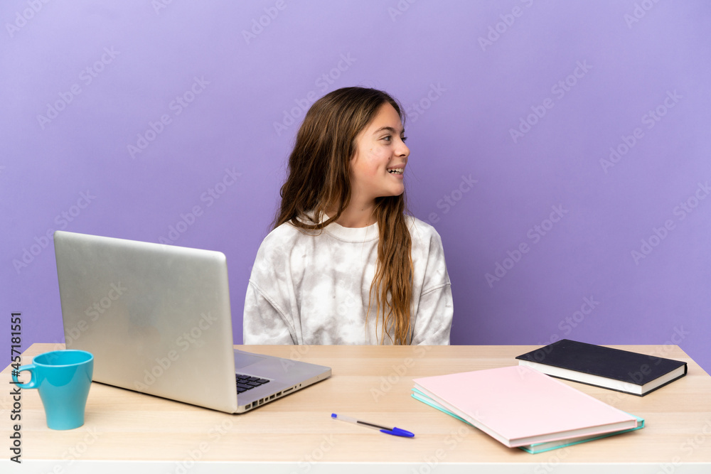 Little student girl in a workplace with a laptop isolated on purple background laughing in lateral position Little student girl in a workplace with a laptop isolated on purple background laughing in lateral position