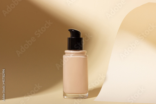 Foundation in a glass bottle on a background with shadows. Face corrector on beige background with copy space. Packaging mockup with copy space