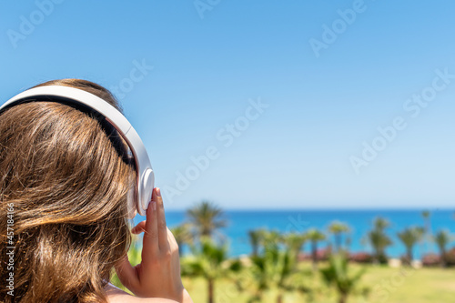 Alone woman on a beach in headphones listen music looking on the sea and palm trees. Female relaxation at summer vacation. Back view