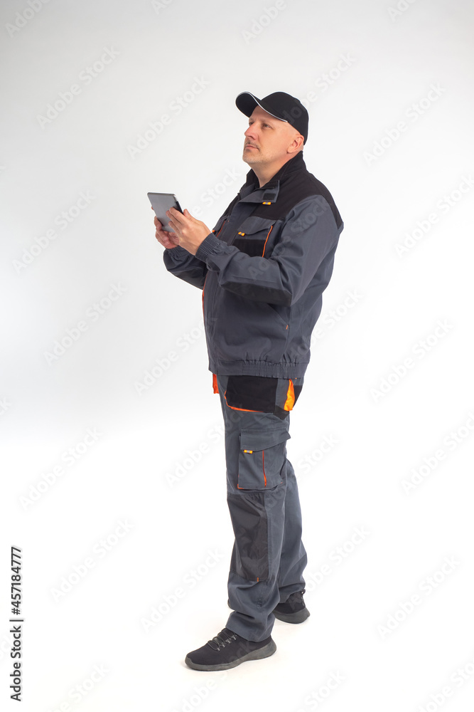 Worker stands on a white background. Portrait of a man in a worker uniform. Worker with electronic tablet looks up. Man works as electrician or repairman. Concept - he uses a tablet to receive orders Worker stands on a white background. Portrait of a man in a worker uniform. Worker with electronic tablet looks up. Man works as electrician or repairman. Concept - he uses a tablet to receive orders