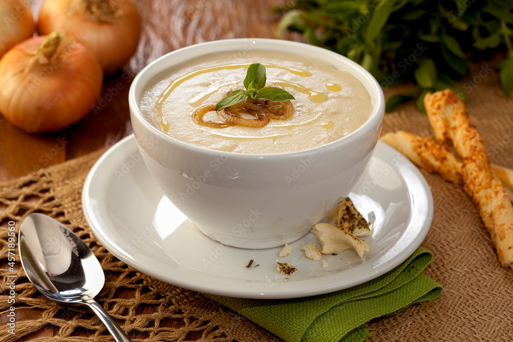 Sopa creme de cebola com folhas de manjericão em tijela de louça em fundo de mesa decorada. Sopa creme de cebola com folhas de manjericão em tijela de louça em fundo de mesa decorada.